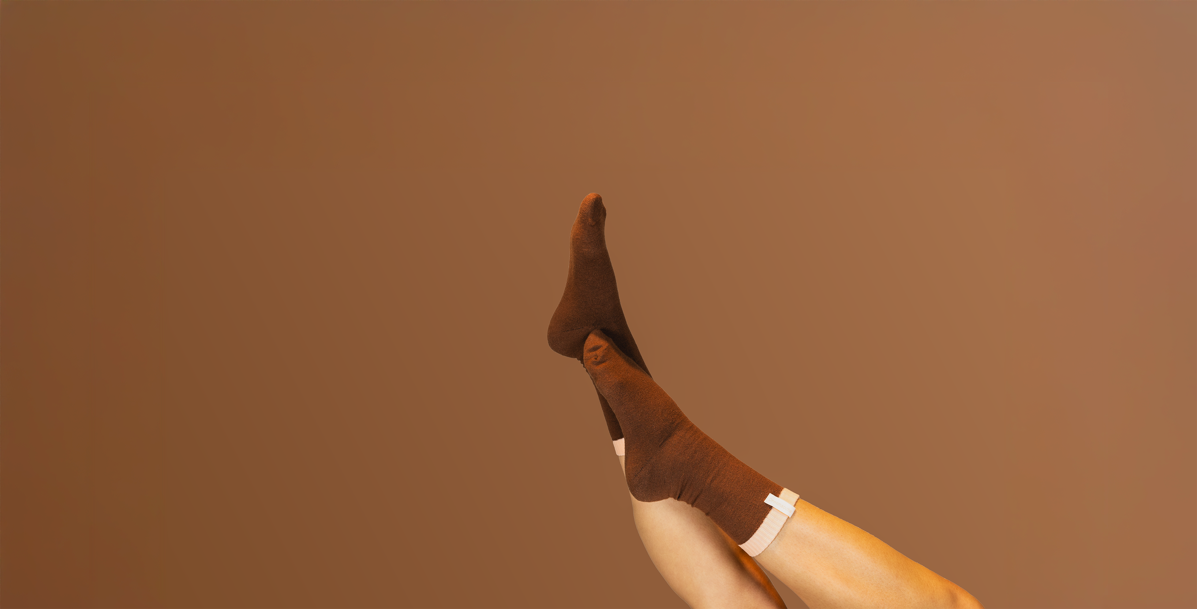 Vrouw die Dreamsocks slaapsokken draagt, met haar benen in de lucht op een bruine achtergrond